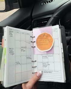 a person is holding a planner in their hand and it's attached to a car steering wheel