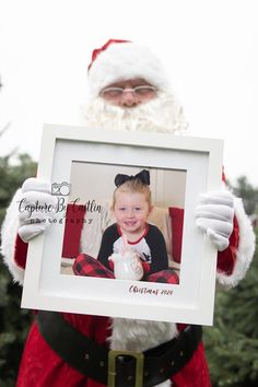 a man dressed as santa claus holding up a picture frame with a child in it