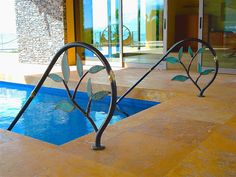 an artistic metal sculpture in front of a swimming pool with blue tiles on the floor