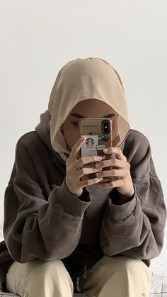 a person sitting on a bench taking a photo with their cell phone while wearing a hoodie