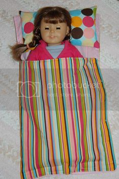 a doll laying on top of a colorful striped bed spread with pillows and pillow cases