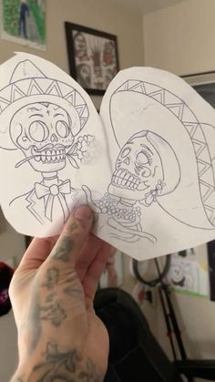 a person holding up two paper cut outs with skulls on them, one is wearing a mexican hat and the other has a skull