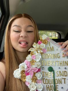 a woman in a car with flowers on her head holding up a sign that says i am coming everything they said couldn't have