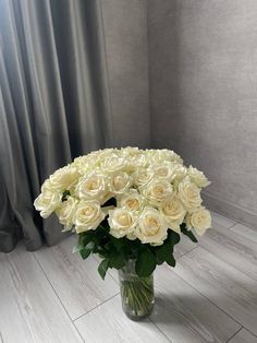 a vase filled with white roses sitting on top of a wooden floor next to a window