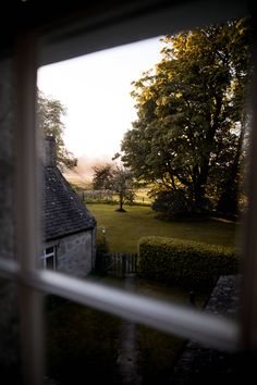 an open window looking out onto a grassy field and treed area with a house in the distance