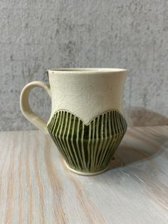 a white and green coffee cup sitting on top of a wooden table next to a wall