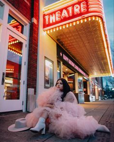 a woman sitting on the ground in front of a theater wearing a pink dress and high heels