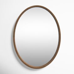 a round mirror hanging on the wall next to a white wall with a wooden frame