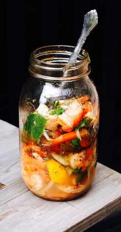 a glass jar filled with food sitting on top of a wooden table next to a spoon