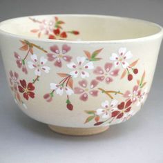 a white bowl with pink and red flowers painted on the side, sitting on a gray surface