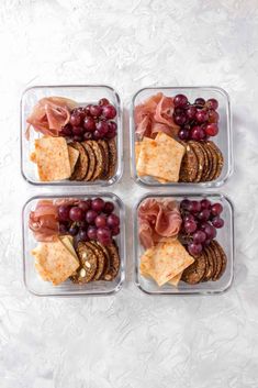 four plastic containers filled with crackers, grapes and cheese on top of a white surface