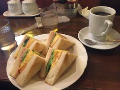 a white plate topped with sandwiches next to a cup of coffee