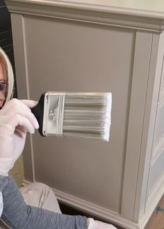 a woman in white gloves is holding a paint brush and painting the side of a cabinet