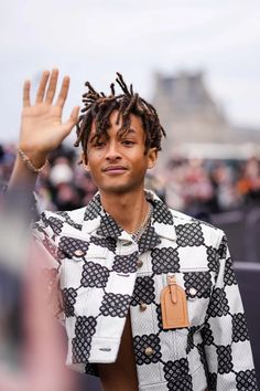 a man with dreadlocks standing in front of a crowd holding his hand up