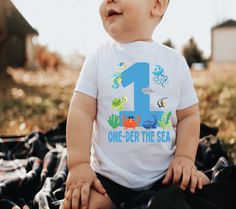 a baby sitting on top of a blanket wearing a one year t - shirt with an ocean theme