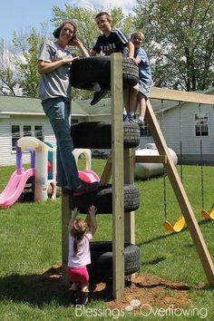 a man and two children playing on a wooden playground set with tire tires in the grass