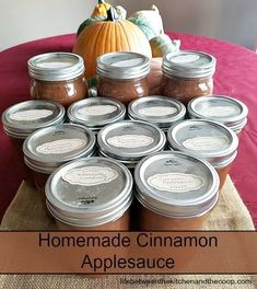 homemade cinnamon applesauce in jars sitting on a table with pumpkins behind it