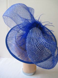 "* Bring in a little excitement to your fashion this season with this bright blue Sinamay hat designed with one gigantic netted bow. Accented with matching Ostrich feathers this is an eye catcher. * The hat is oval with a 2-1/2\" brim and with the clip on the inside can be positioned as desired. The pictures show just two positions as my model has no hair! * This particular design is off the center of the head and can be worn on either the right or left side of the head. * It is light weight, we Blue Summer Hat With Feathers, Blue Party Hat With Feather Trim, Blue Feathered Summer Hat, Blue Feathered Fascinator Hat, Blue Feathered Hat Fascinator, Lavender Bunny, Sinamay Hat, Ladies Luncheon, Holiday Dinner Party