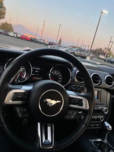 the steering wheel and dashboard of a car in a parking lot with other cars behind it