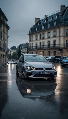 a silver car parked in front of a building on a wet street with buildings behind it