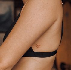 a woman with a small heart tattoo on her left side arm and chest, wearing a black bra