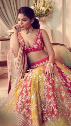 a woman in a red and yellow lehenga sitting on a chair with flowers