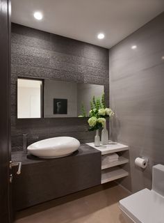 a white sink sitting on top of a counter next to a toilet and a vase with flowers in it