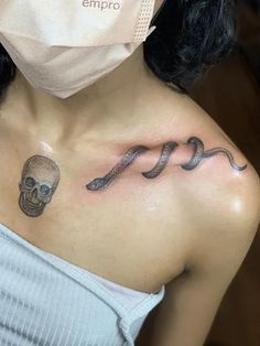 a woman with a skull and snake tattoo on her chest is wearing a face mask