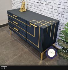 a black and gold dresser sitting next to a brick wall with a golden statue on top