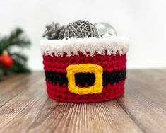 a red and white crocheted basket with yarn in it on top of a wooden table