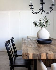 a dining room table with a vase on top of it next to two chairs and a chandelier