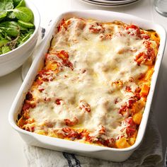 a casserole dish with cheese and spinach on the side next to a salad