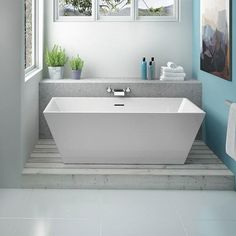 a white bath tub sitting next to a window in a blue and white bathroom with potted plants