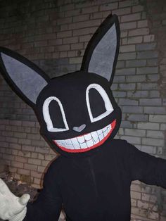 a person wearing a black cat mask and holding something in one hand while standing next to a brick wall