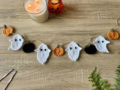 crocheted ghost garland with pumpkins and candles on wooden table next to candle