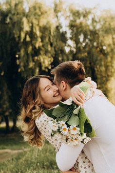 a man and woman kissing each other in front of some trees with sunflowers