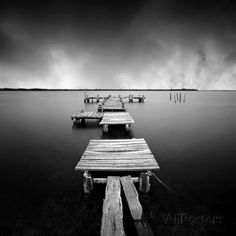 black and white photograph of dock on water with storm clouds in the sky over it