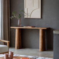 a wooden table with a vase on it next to a chair and a painting hanging on the wall