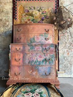 an old dresser with flowers painted on the top and bottom, sitting next to another piece of furniture