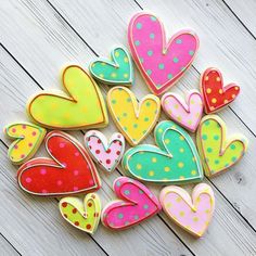 decorated cookies are arranged in the shape of hearts on a white wooden surface with polka dots