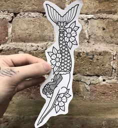 a hand holding up a sticker with an image of a fish and flowers on it