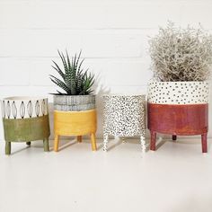 three planters with plants in them sitting on a white table next to a brick wall