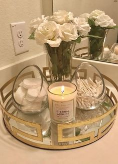 a candle and some white flowers on a table in front of a mirror with two vases