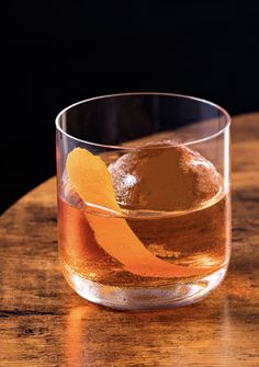 an old fashioned glass with some orange peels in it sitting on a wooden table