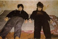 two young men laying on top of a bed next to each other in front of a wall