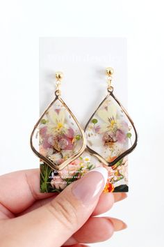 a hand holding up a pair of earrings with flowers on the front and back of it