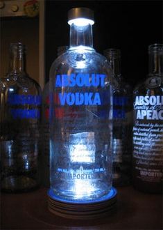 an illuminated vodka bottle sitting on top of a wooden table next to other liquor bottles