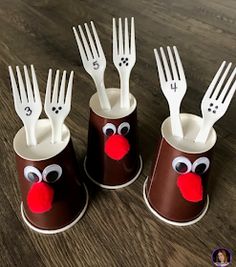 four plastic cups with forks sticking out of them on a wooden table next to a pair of scissors