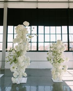 two vases filled with white flowers sitting on top of a floor next to each other