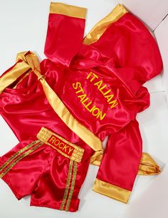 a red and gold boxing suit laying on top of a white floor next to a pair of gloves